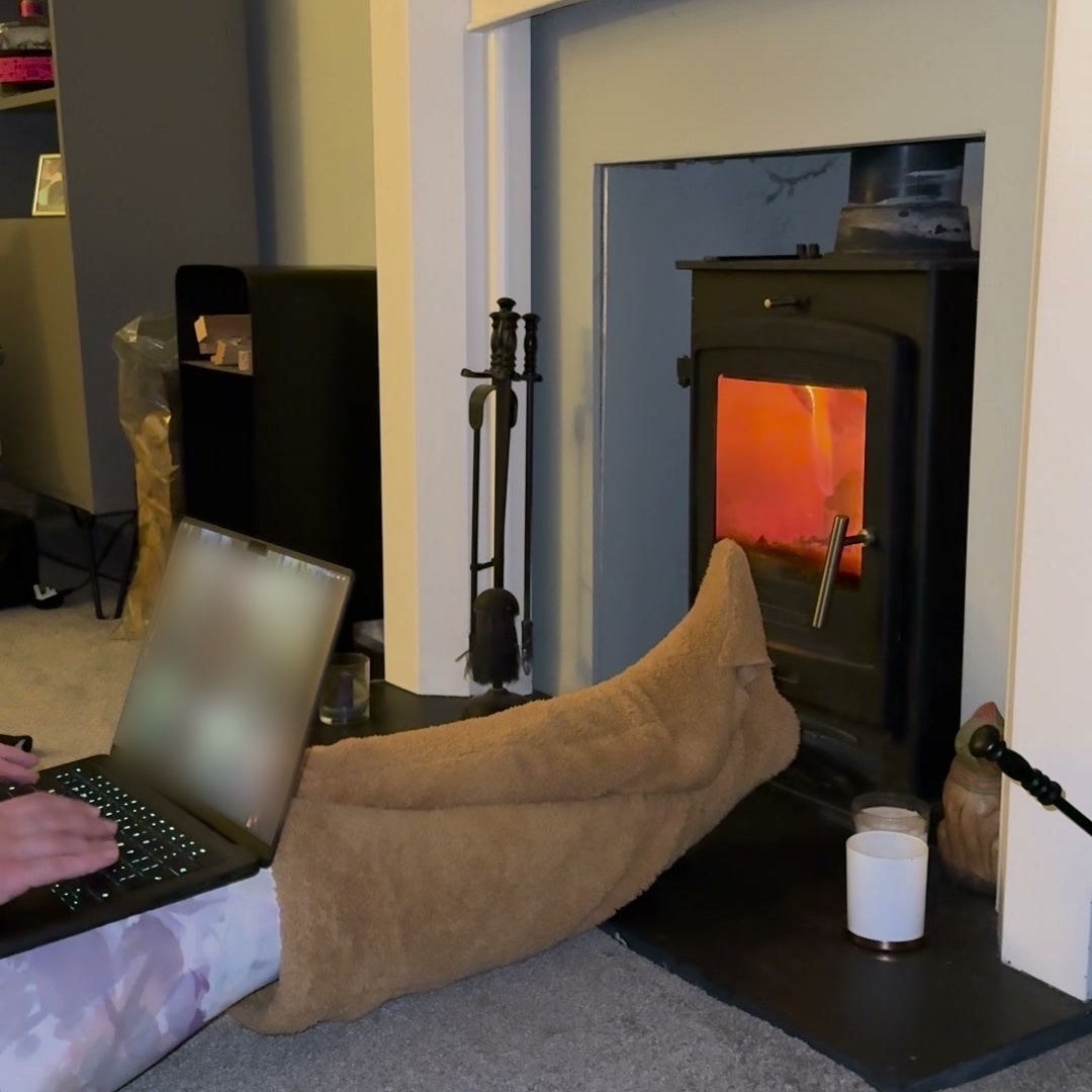 Woman typing on a laptop balanced on her knees, legs in camel teddy fleece over-the-knee leg warmers