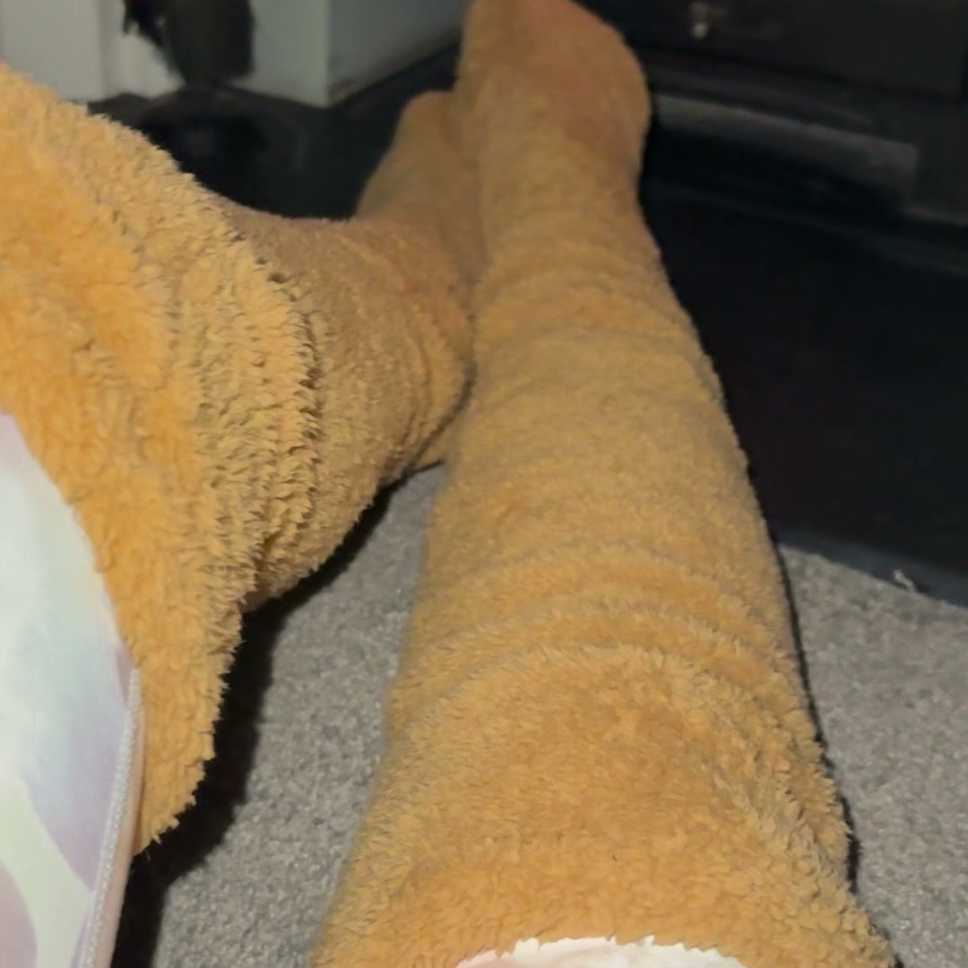 Both legs in camel teddy fleece over-the-knee leg warmers, the plush pile visible along the full length of the calf